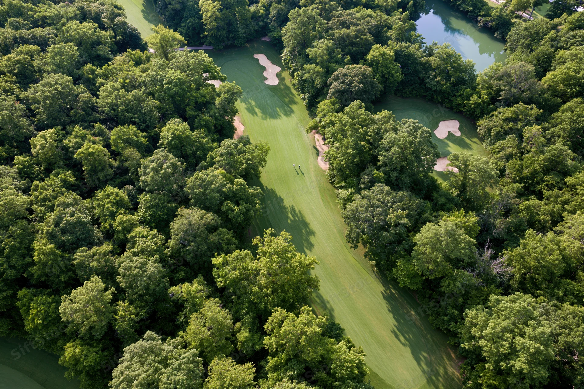 Aerial view of a golf course fairway winding through dense trees with water and sand traps visible