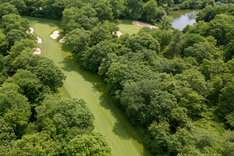 Aerial view of a golf course fairway winding through dense trees with sand traps and a pond nearby