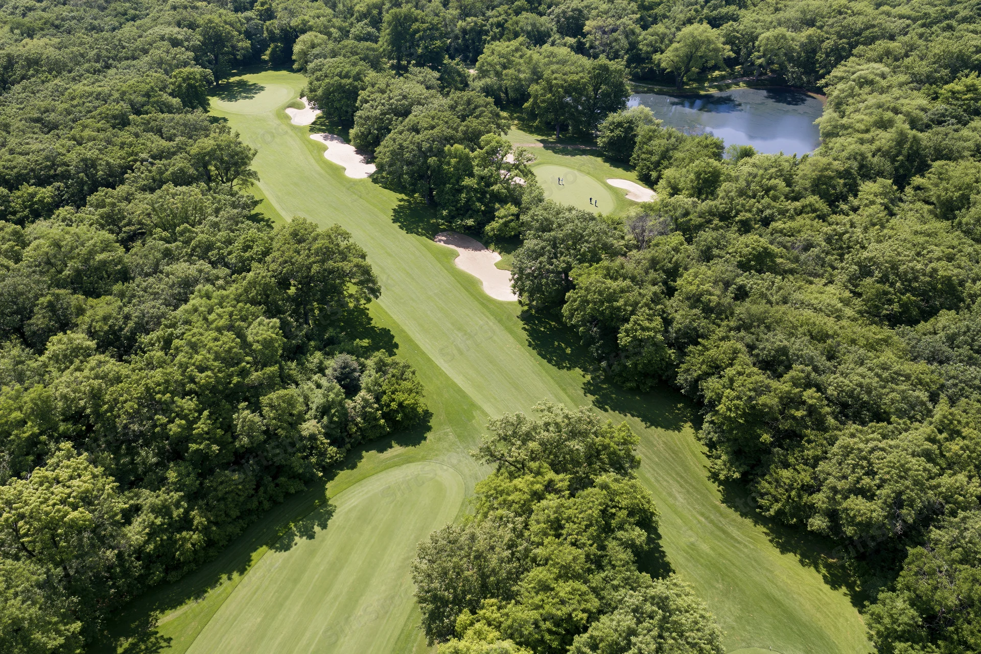 Aerial view of a golf course fairway winding through dense trees with a pond and sand traps visible