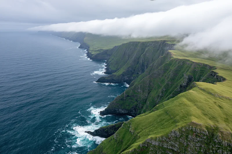 Aerial view of rugged volcanic coastline with steep green cliffs meeting the ocean under cloudy sky
