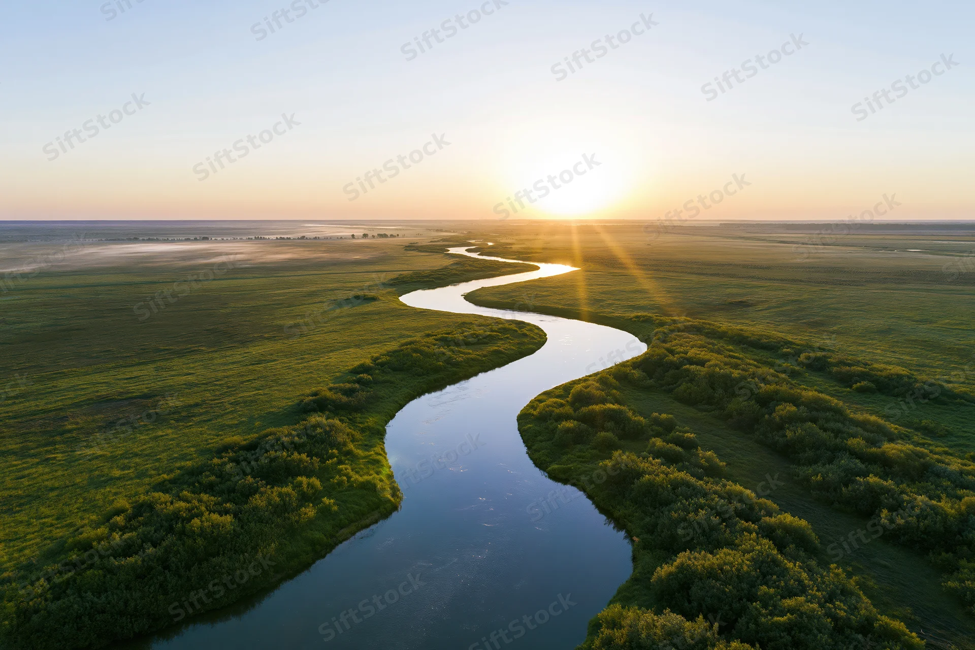 Aerial view of a winding river snaking through flat green wetlands at sunset