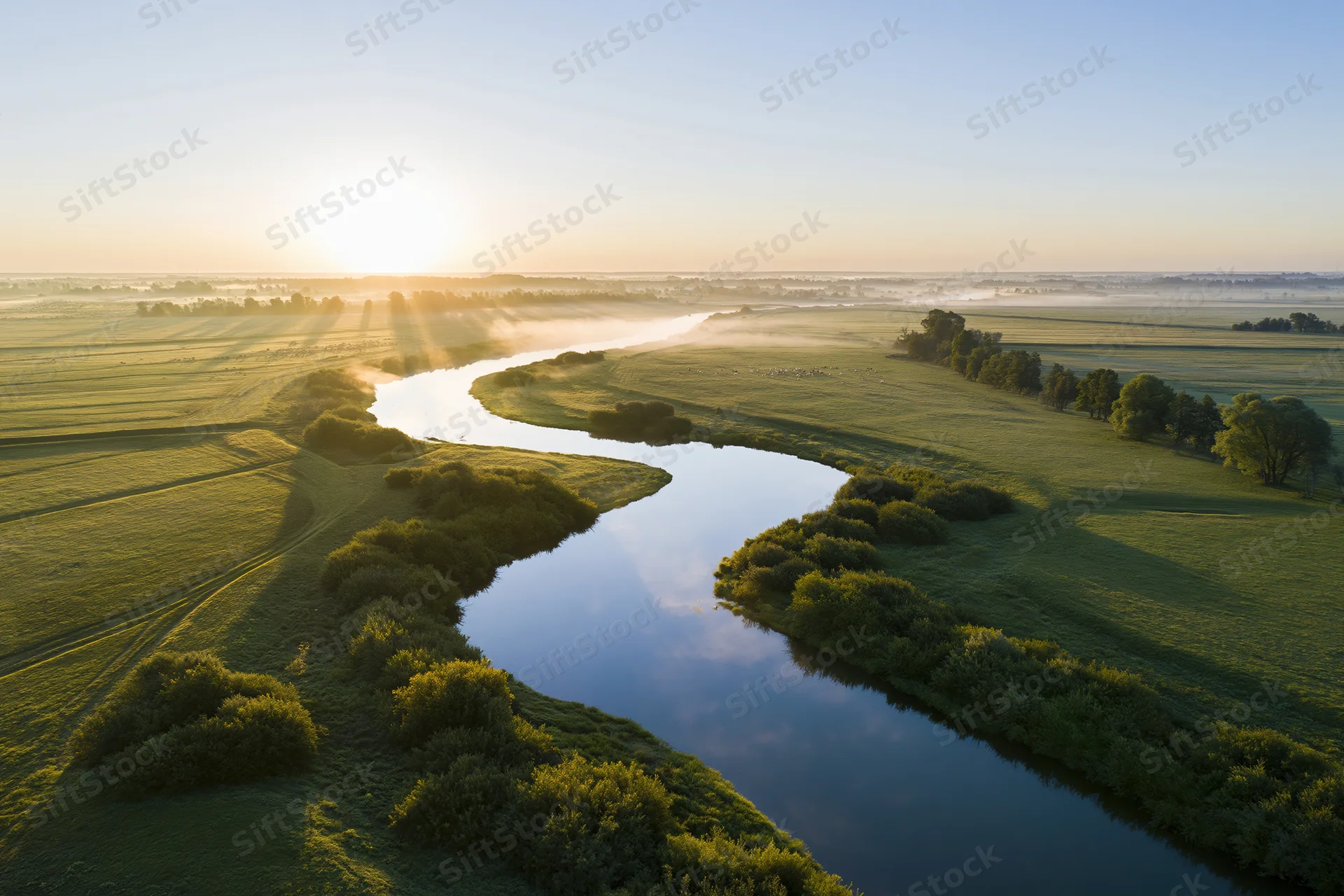 Aerial view of a winding river snaking through flat green fields at sunrise