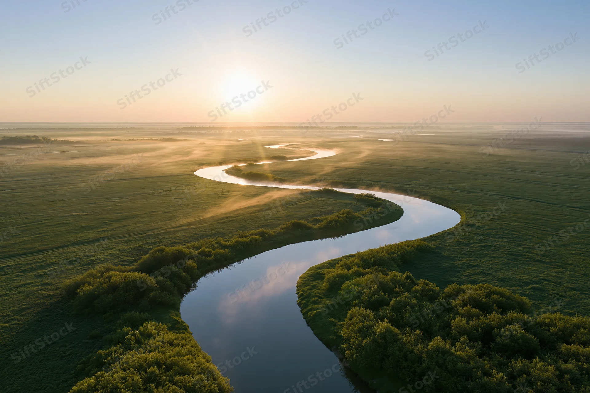 Aerial view of a winding river snaking through flat green fields at sunrise