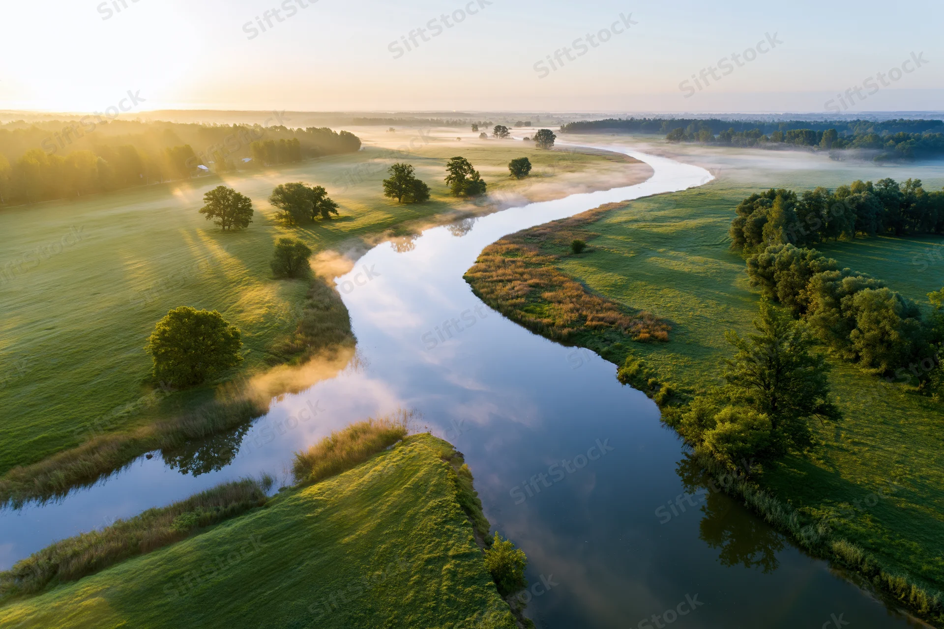 Aerial view of a winding river flowing through green meadows at sunrise