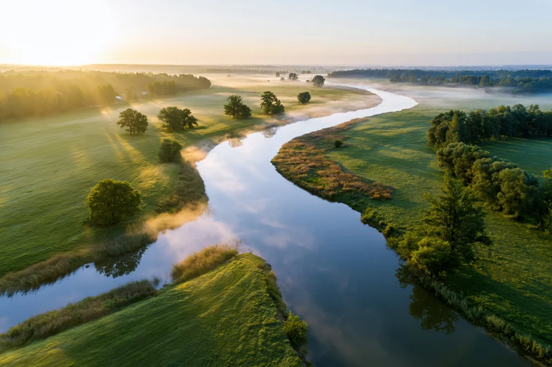 Aerial view of a winding river flowing through green meadows at sunrise