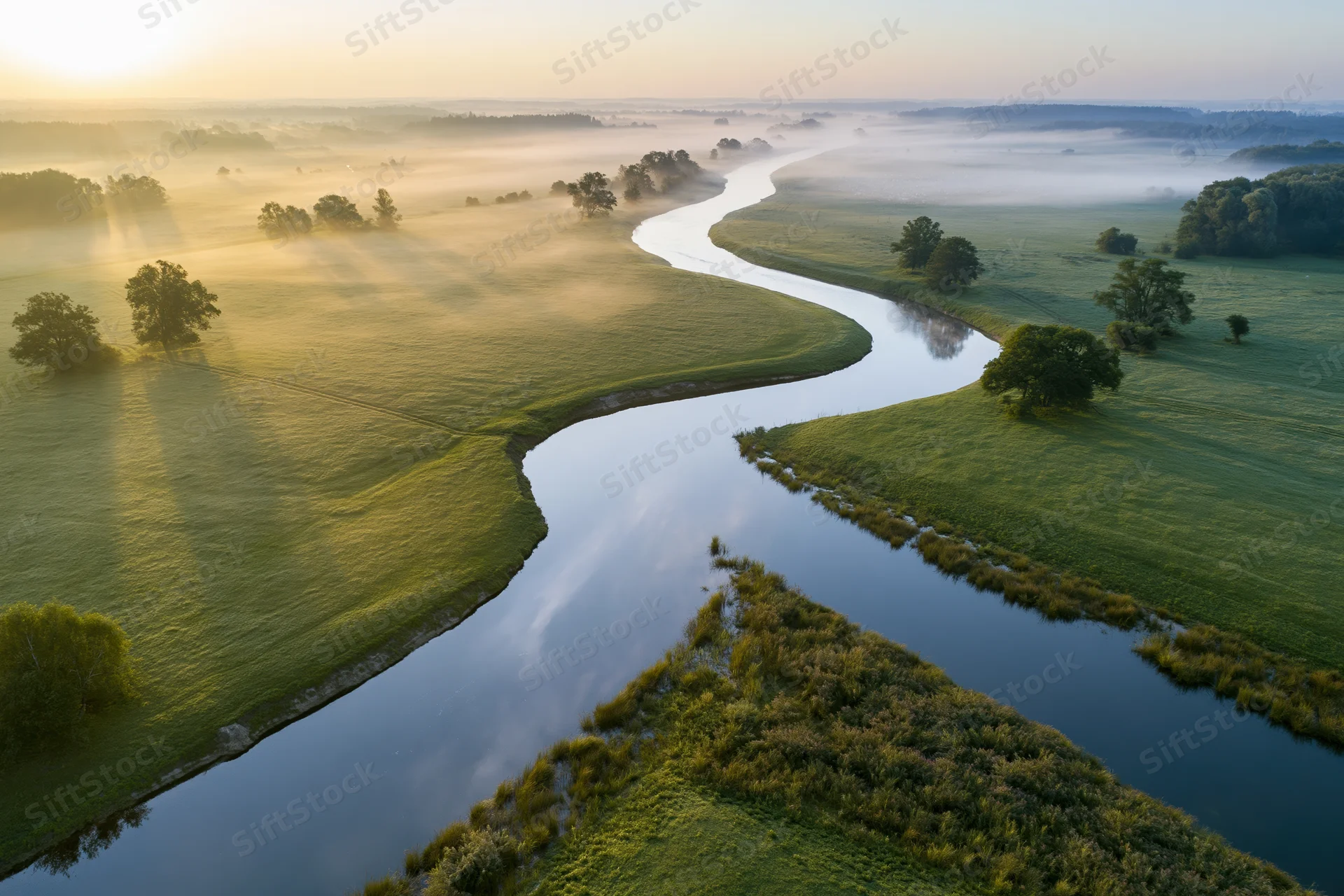 Aerial view of a winding river snaking through flat green meadows at sunrise