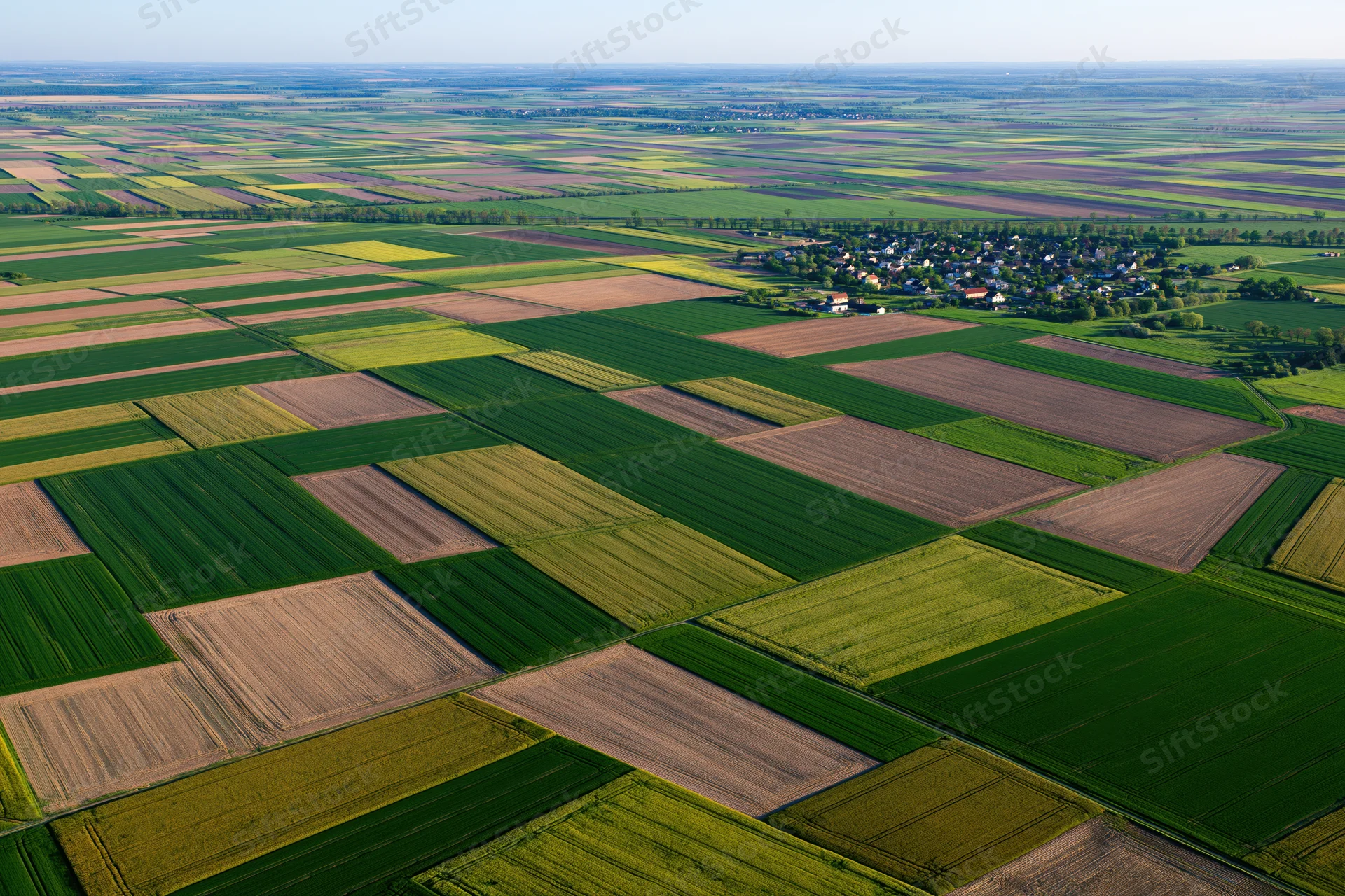 Aerial view of patchwork agricultural fields stretching to the horizon with a small village in the distance