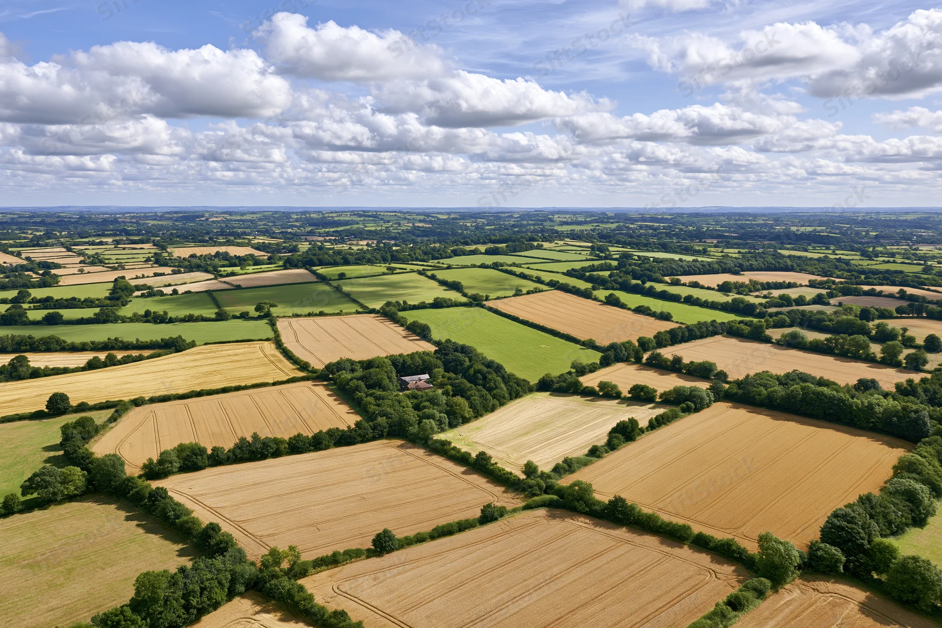 Aerial view of patchwork farmland in rolling english countryside under blue sky with white clouds