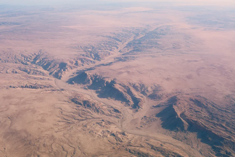 Aerial view of vast arid desert landscape with rocky canyons and ridges from high altitude