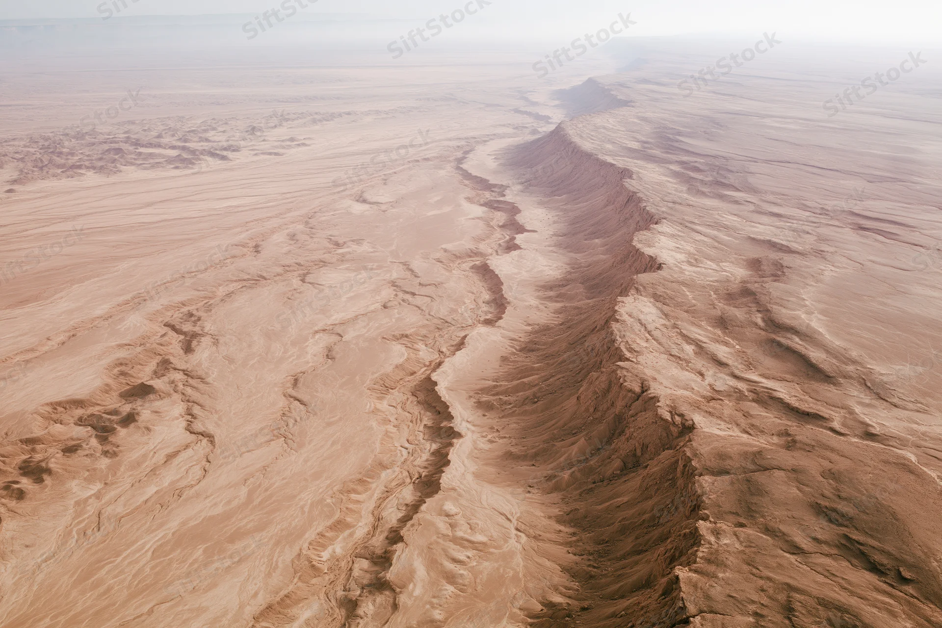 Aerial view of a vast arid desert landscape with deep canyons and eroded rock formations from high altitude