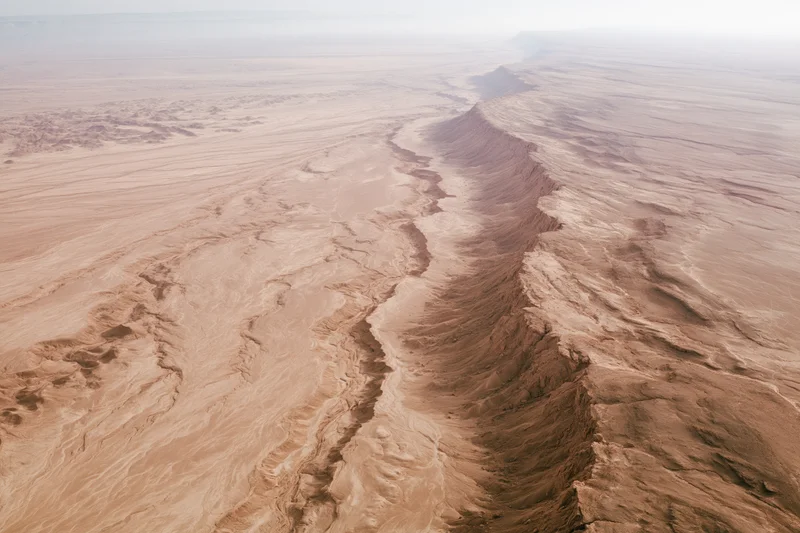 Aerial view of a vast arid desert landscape with deep canyons and eroded rock formations from high altitude