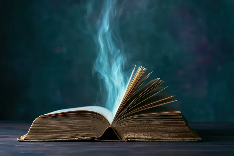Open old weathered hardcover book with blue smoke rising from pages on dark wooden surface