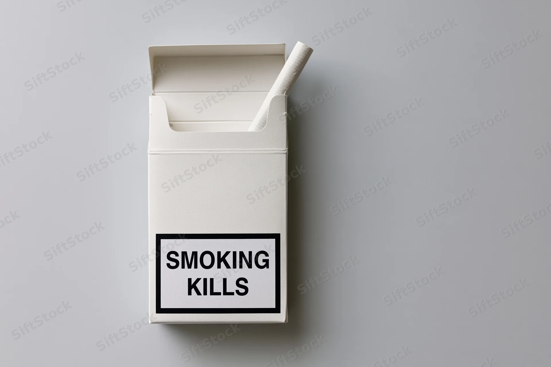 Open white cigarette pack with one cigarette sticking out, warning label reading smoking kills, flat lay on gray surface