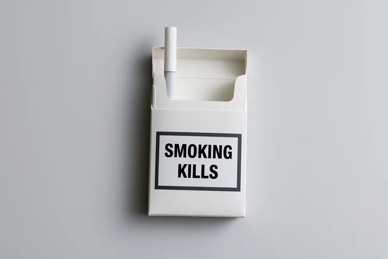 Open white cigarette pack with one cigarette sticking up and smoking kills warning label on plain gray background