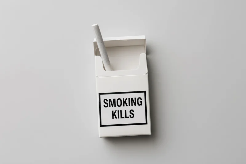 Open white cigarette pack with one cigarette sticking up and smoking kills warning label on plain gray background