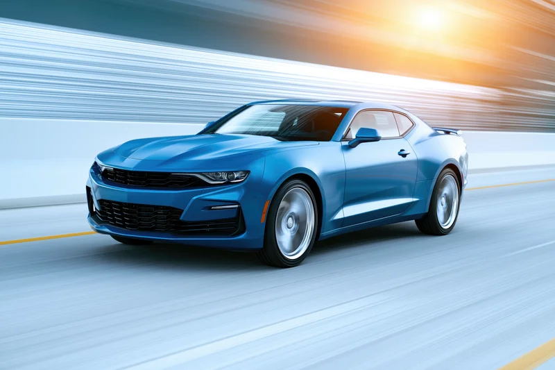 Blue chevrolet camaro muscle car driving at speed on open road with motion blur and sunlight