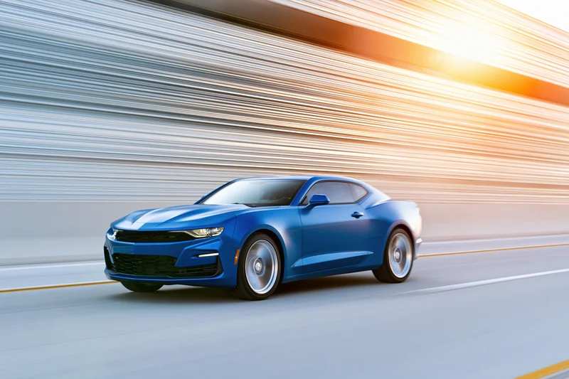 Blue chevrolet camaro muscle car driving at speed on a highway with motion blur