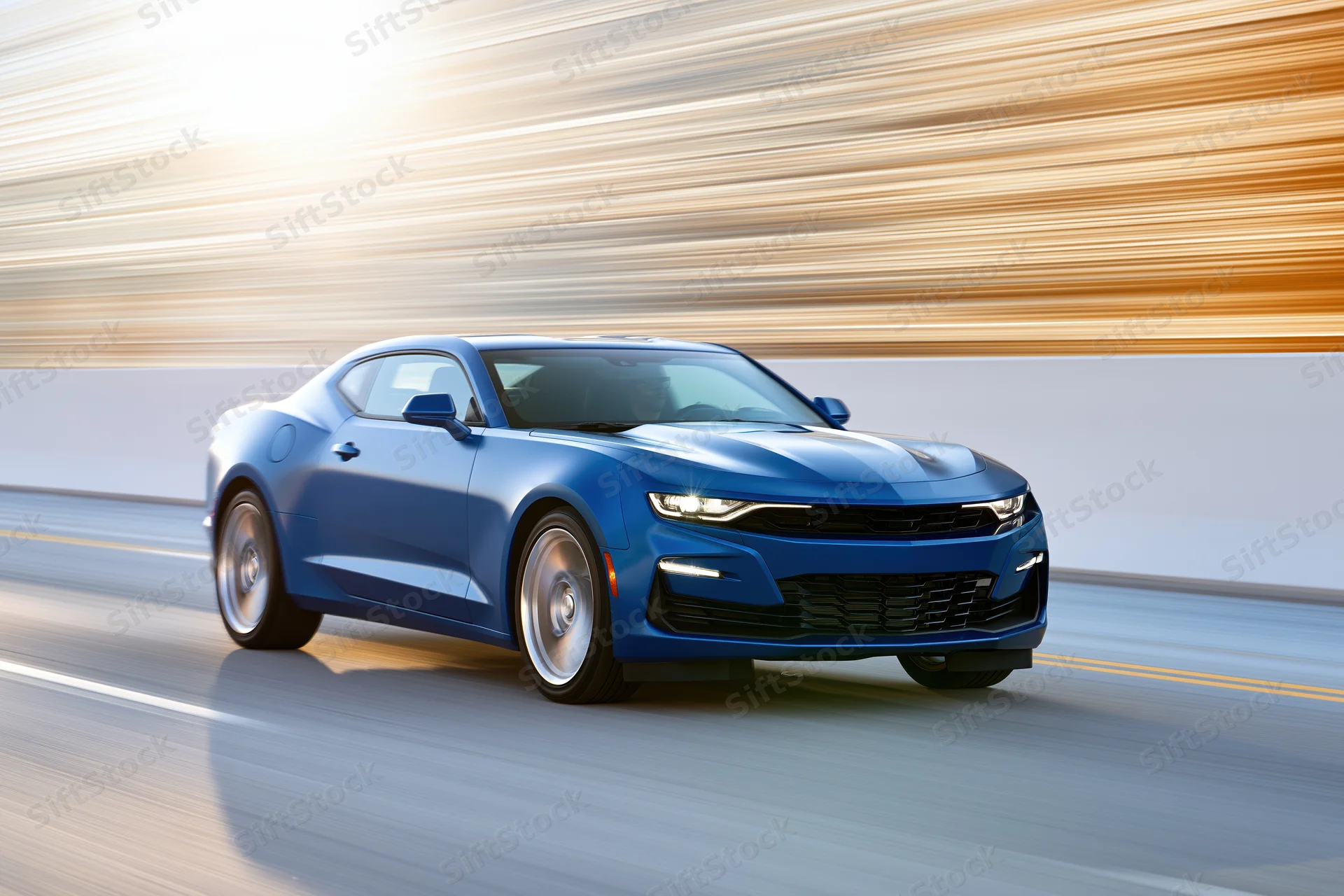 Blue chevrolet camaro muscle car driving at speed on open highway with motion blur