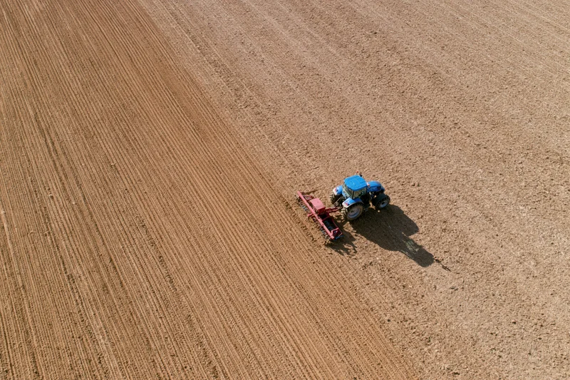Blue tractor pulling a red tillage implement across large field