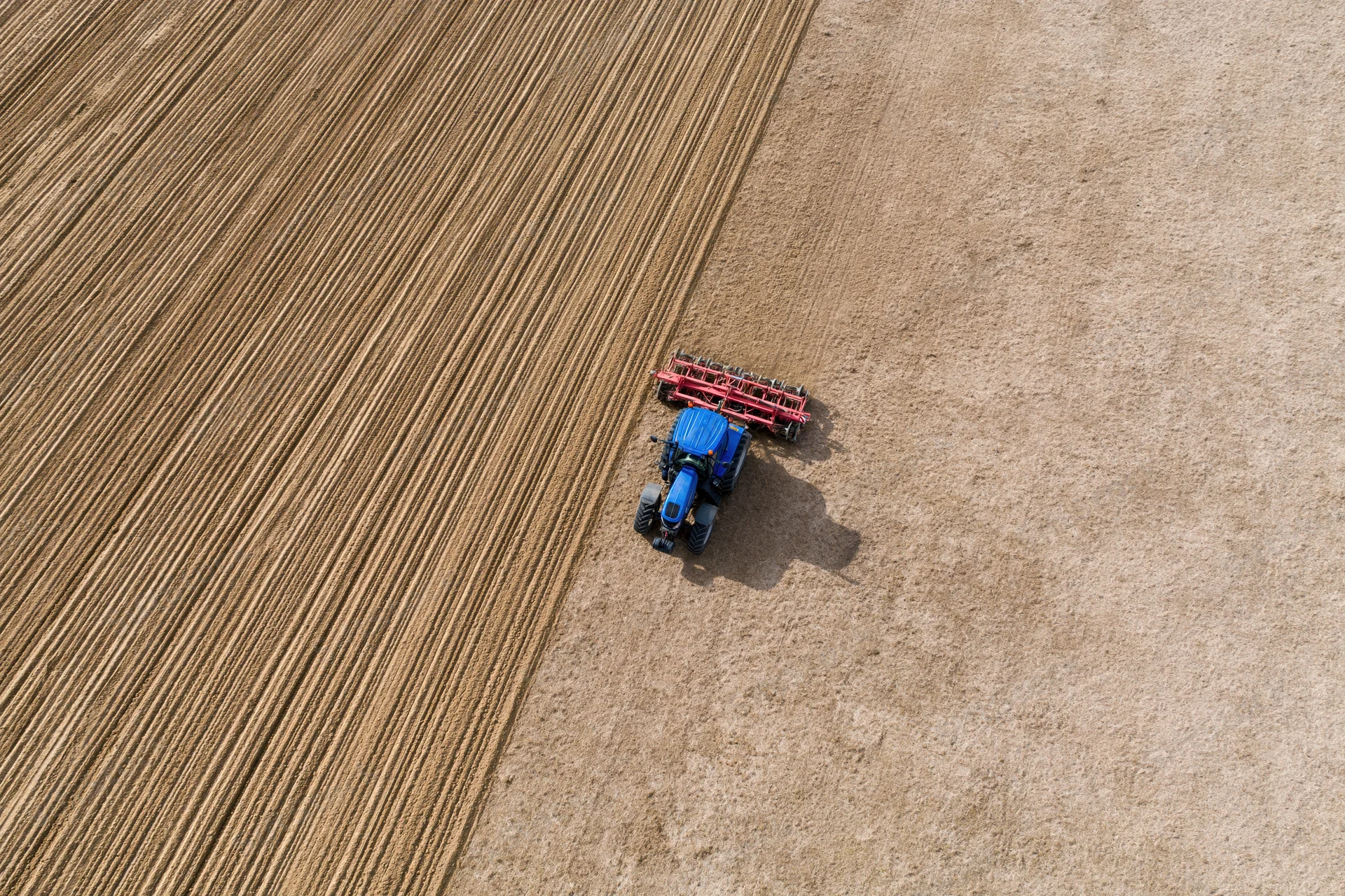 Blue tractor pulling red tillage implement across large agricultural field