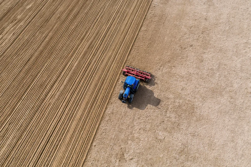 Blue tractor pulling red tillage implement across large agricultural field