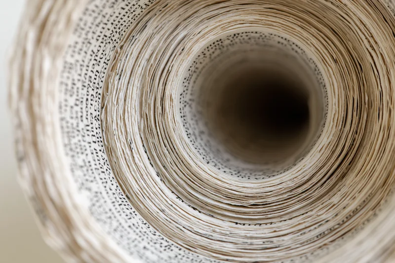 Tightly rolled book pages forming a spiral tunnel with printed text visible along the edges