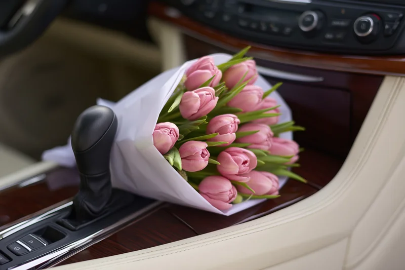 Bouquet of pink tulips wrapped in white paper resting on car center console
