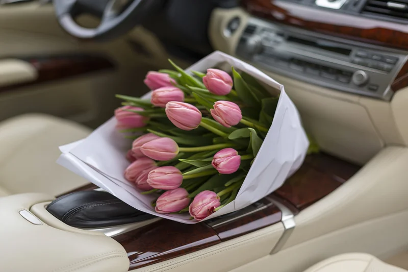 Bouquet of pink tulips wrapped in white paper resting on car center console