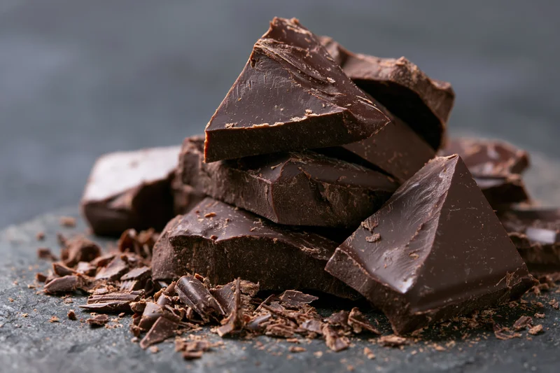 Broken dark chocolate chunks piled roughly on a slate surface