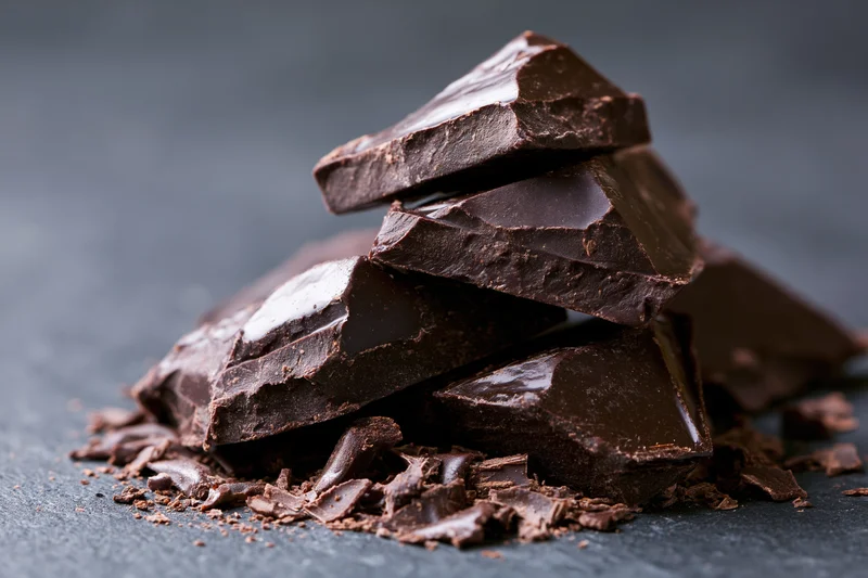 Broken dark chocolate chunks stacked in a rough pile on a dark slate surface