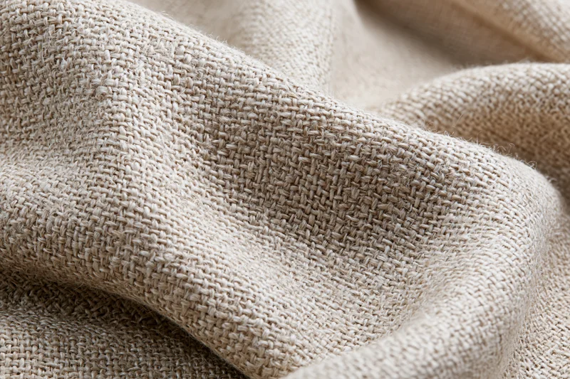 Close-up of natural linen fabric with visible weave and soft folds filling the frame