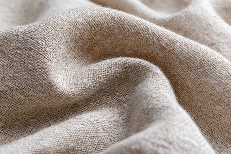 Close-up of natural linen fabric with visible weave and soft folds filling the frame