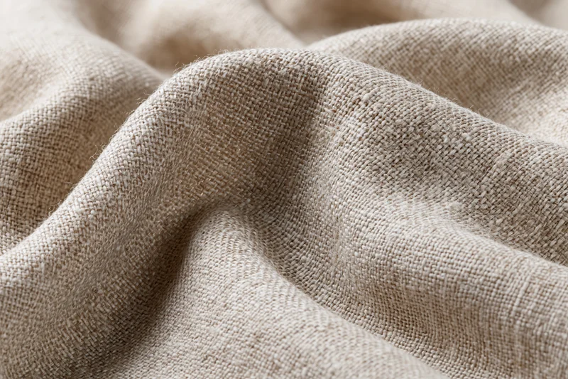 Close-up of natural linen fabric with visible weave and soft folds filling the frame