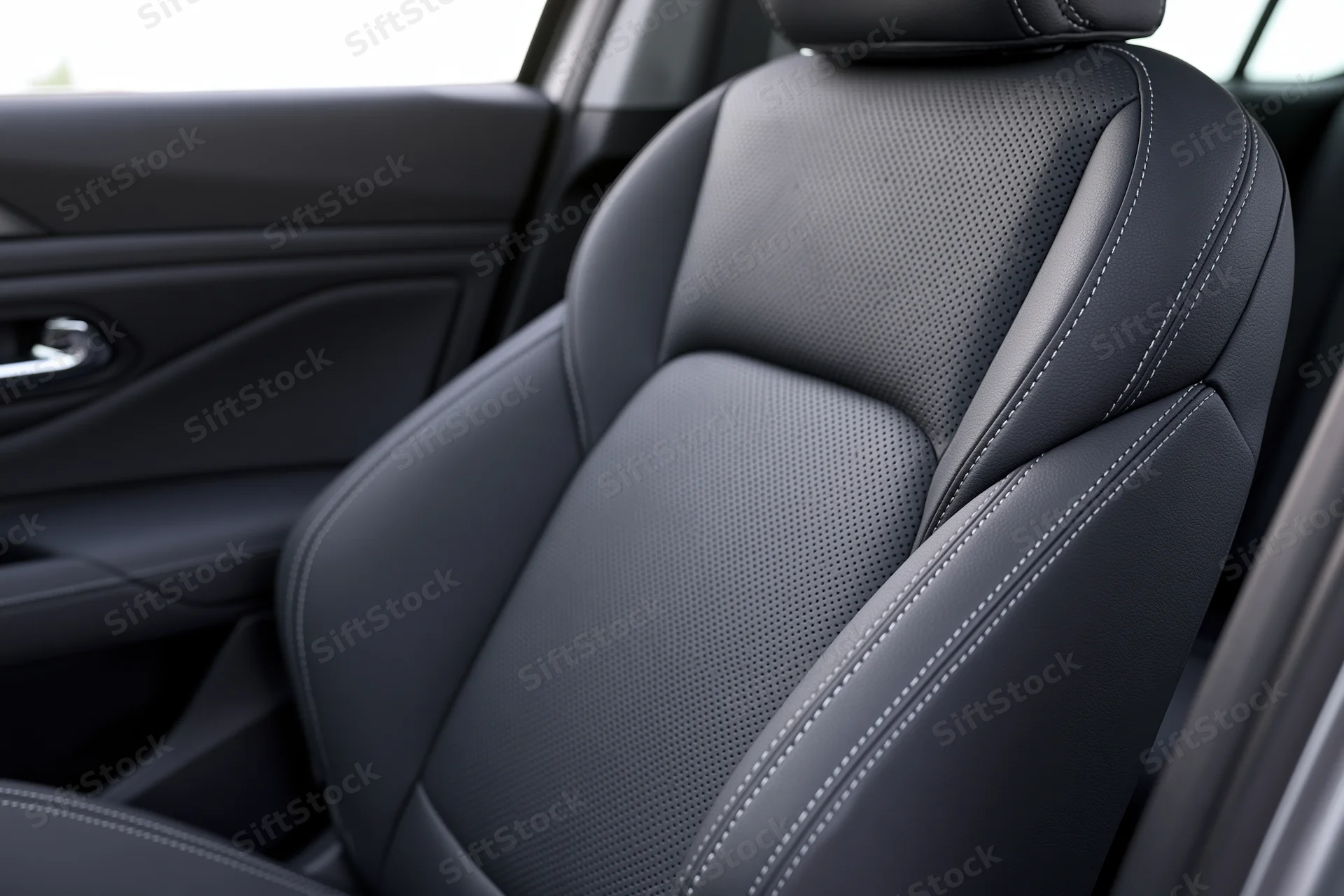 Close-up of a modern car's front passenger seat with black perforated leather upholstery and white stitching inside the cabin