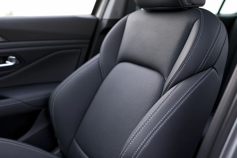 Close-up of a modern car's front passenger seat with black perforated leather upholstery and white stitching inside the cabin