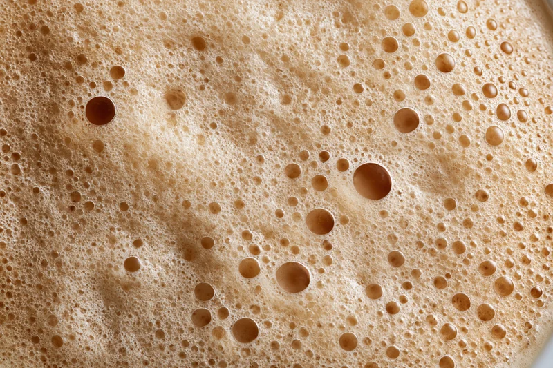 Close-up of coffee foam surface with bubbles and texture filling the frame