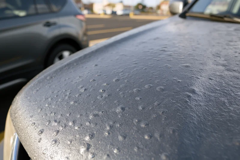 Close-up of hail-damaged car hood in a parking lot during daytime