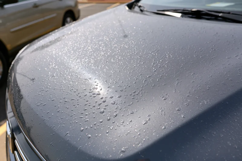 Close-up of water droplets on dark gray SUV hood in daylight parking lot