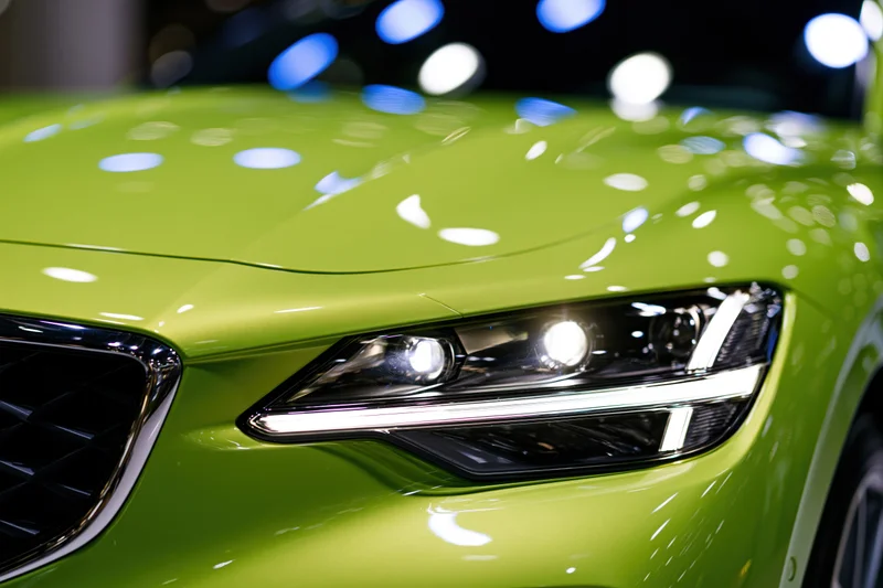 Close-up of a green metallic sports car headlight glowing in a showroom setting