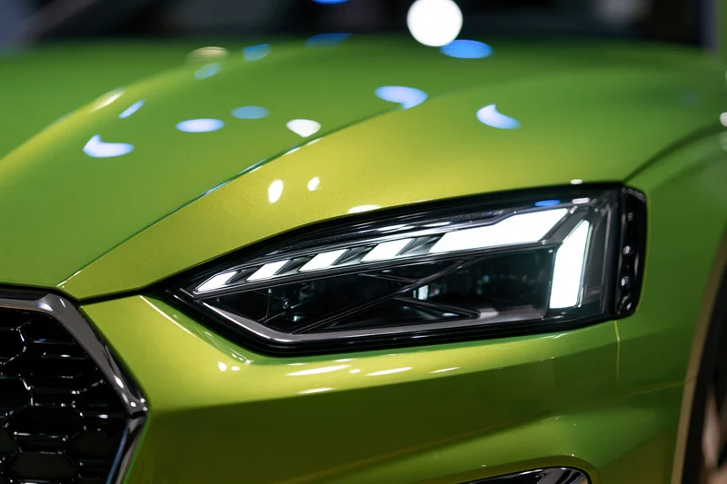 Close-up of a green metallic sports car headlight glowing in a showroom setting