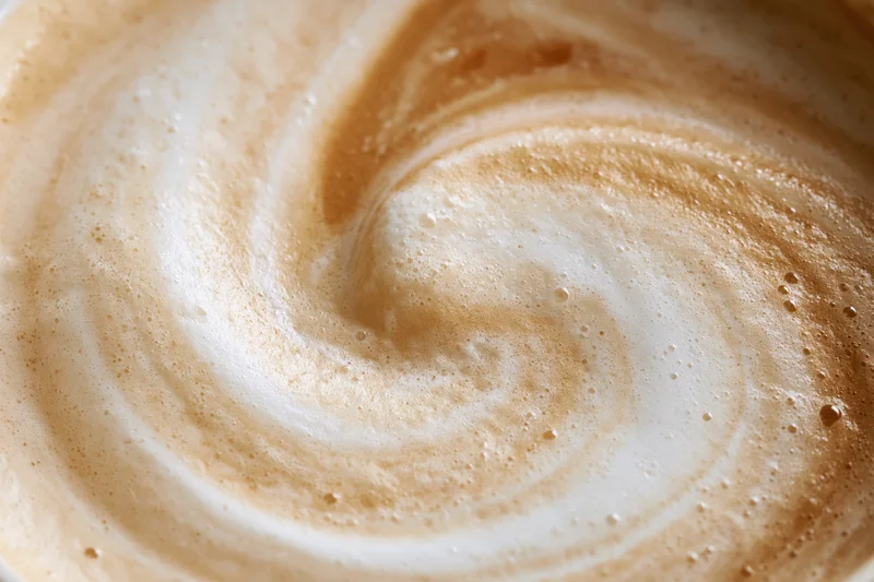 Close-up overhead view of swirling milk foam on a coffee surface
