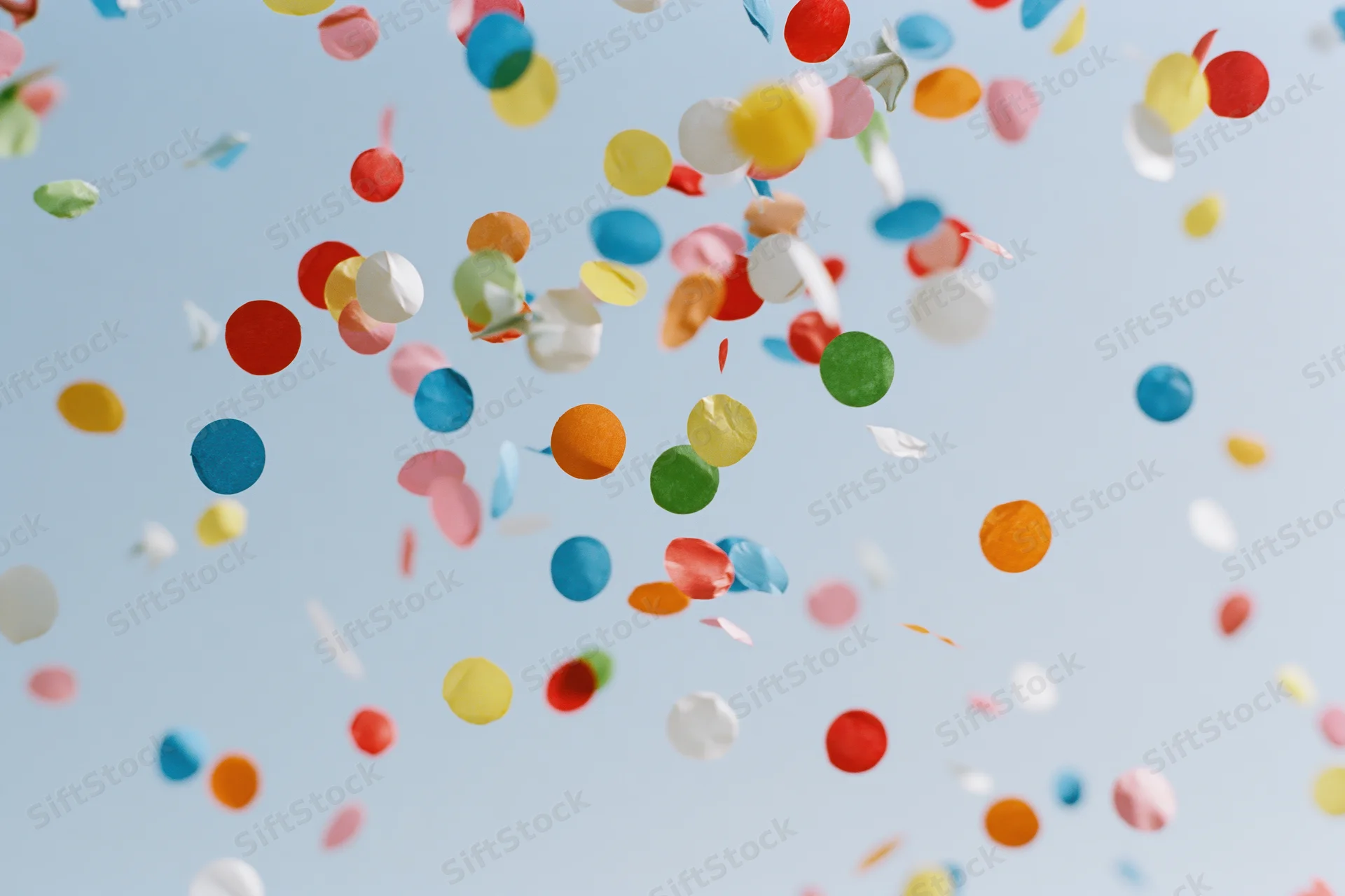 Colorful confetti pieces floating upward against a clear sky
