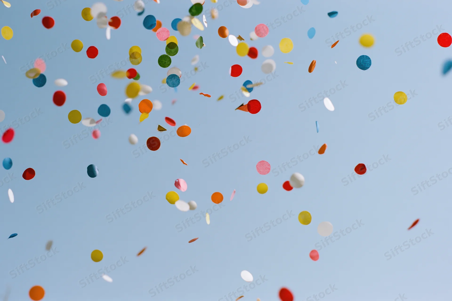 Colorful confetti pieces floating upward against a clear blue sky