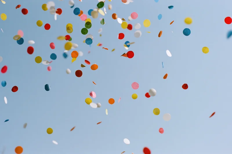 Colorful confetti pieces floating upward against a clear blue sky