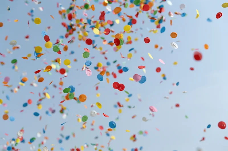 Colorful confetti floating upward against a clear sky during a celebration
