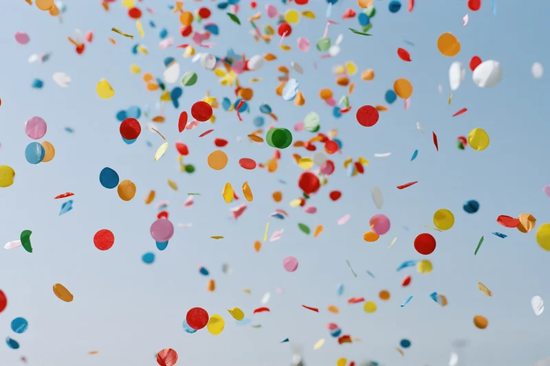 Colorful confetti pieces floating upward against a clear blue sky