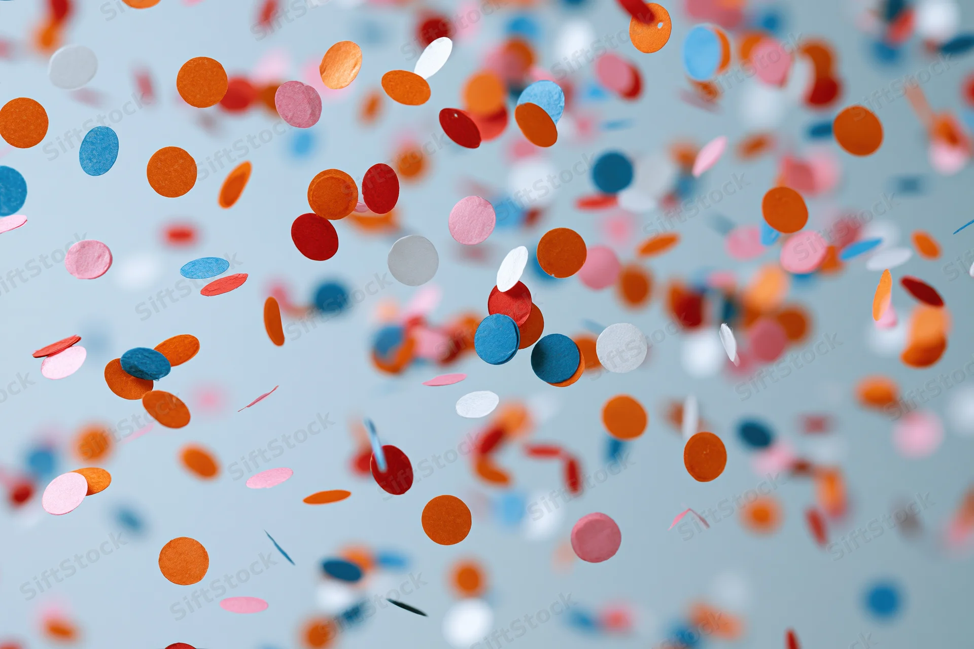 Colorful paper confetti pieces floating and falling midair against a light blue background