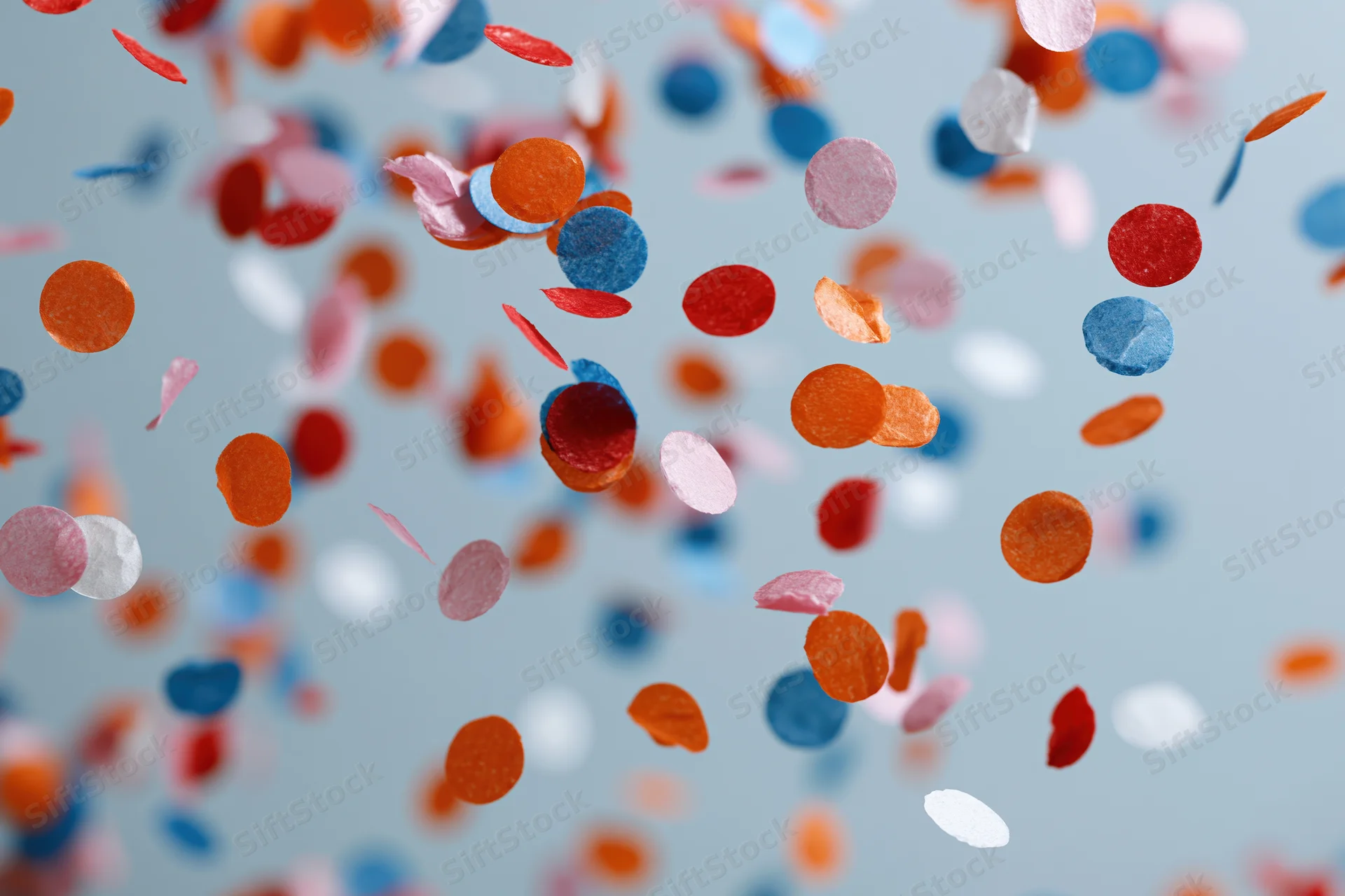 Colorful paper confetti pieces floating and falling midair against a light blue background
