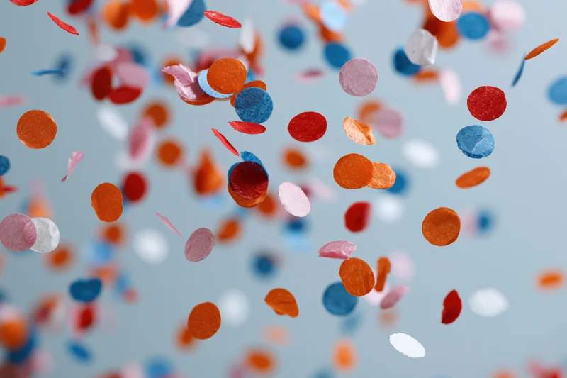 Colorful paper confetti pieces floating and falling midair against a light blue background
