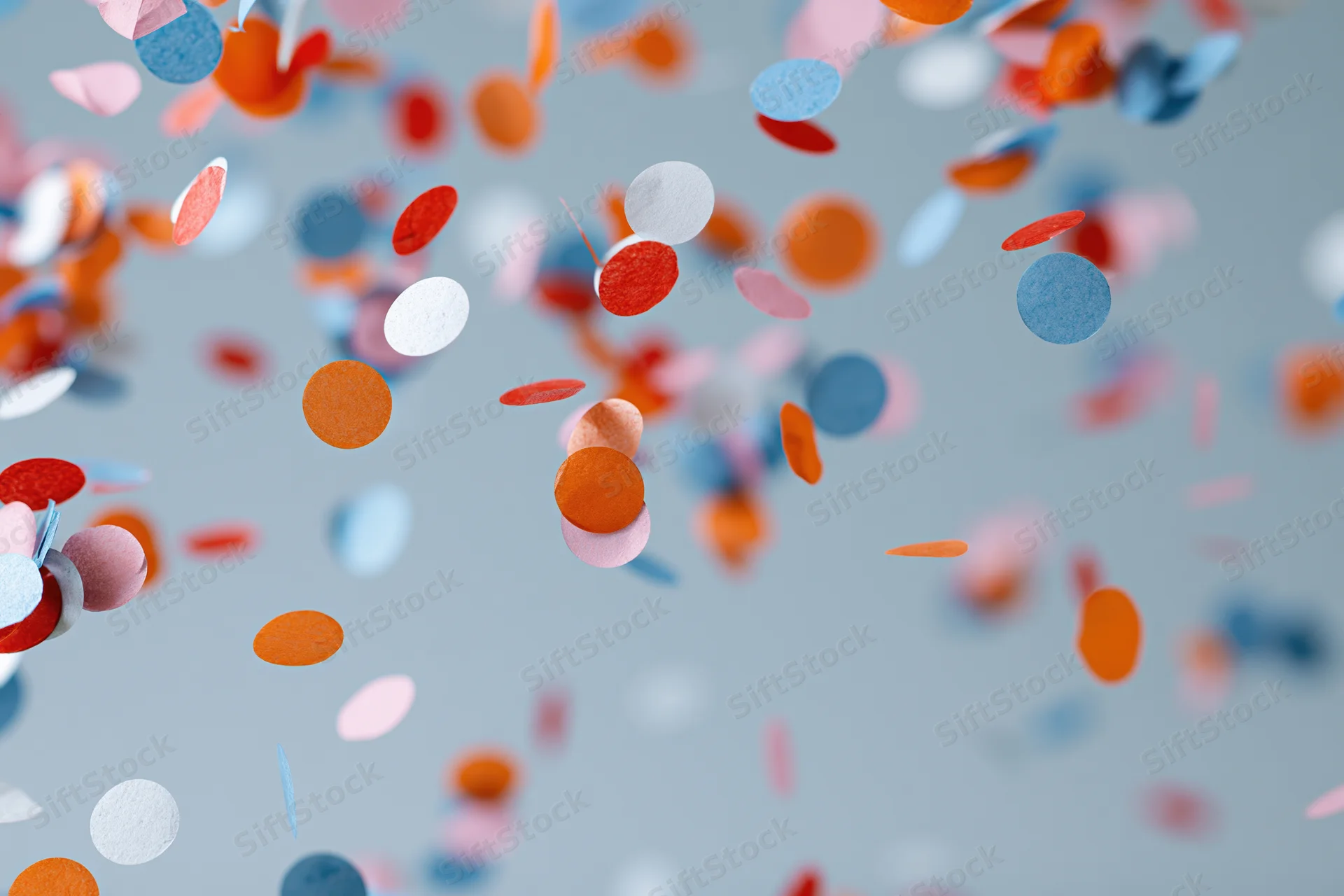 Colorful paper confetti pieces floating and falling midair against a gray background